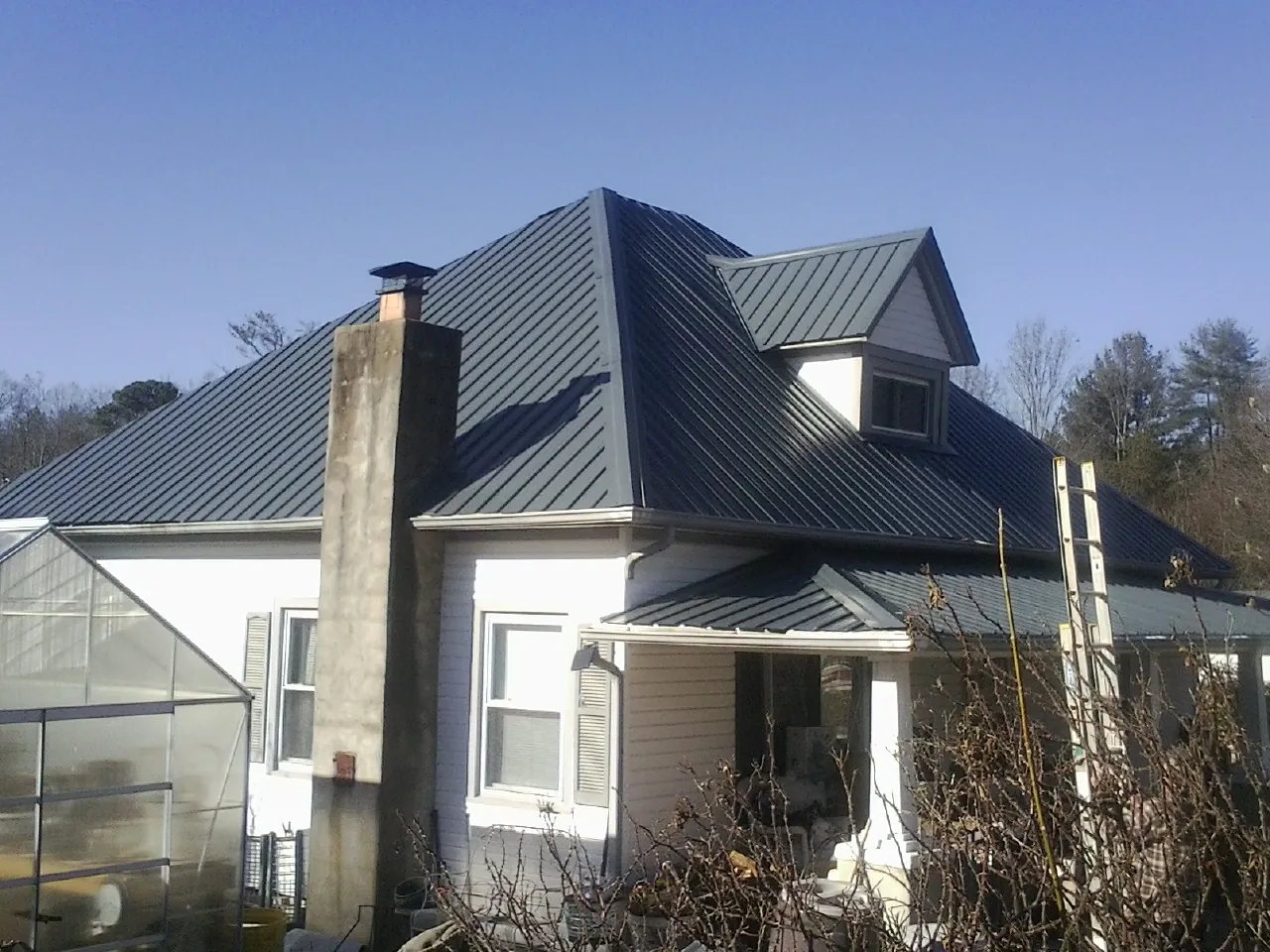 Dark blue standing seam metal roof on a white farmhouse with dormer — Slate & Tile Roof Repair by Roofing Brothers in Maiden