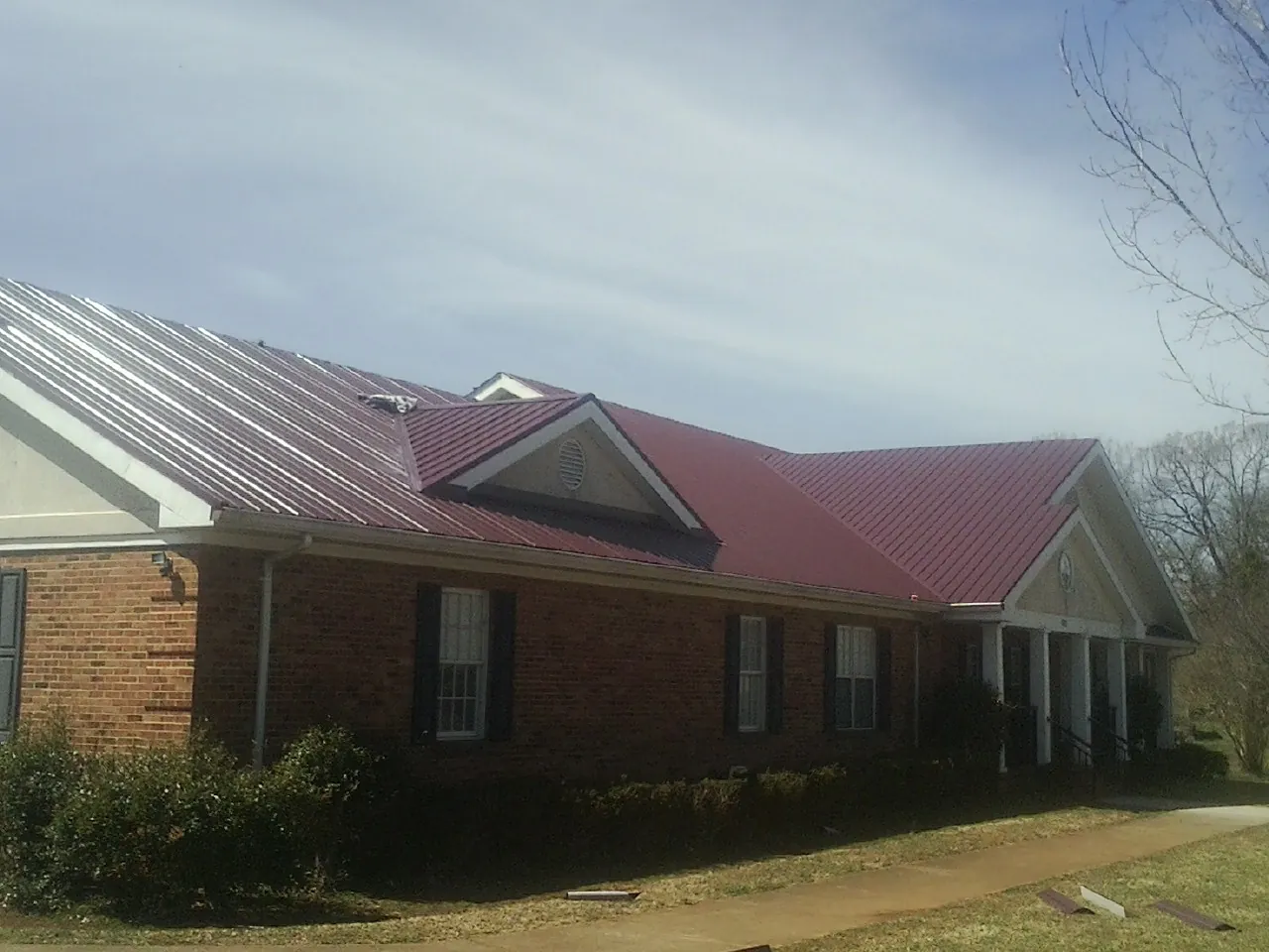 Red metal roof with gabled entries on a long brick building, from a Hail Damage Roof Repair job in Maiden