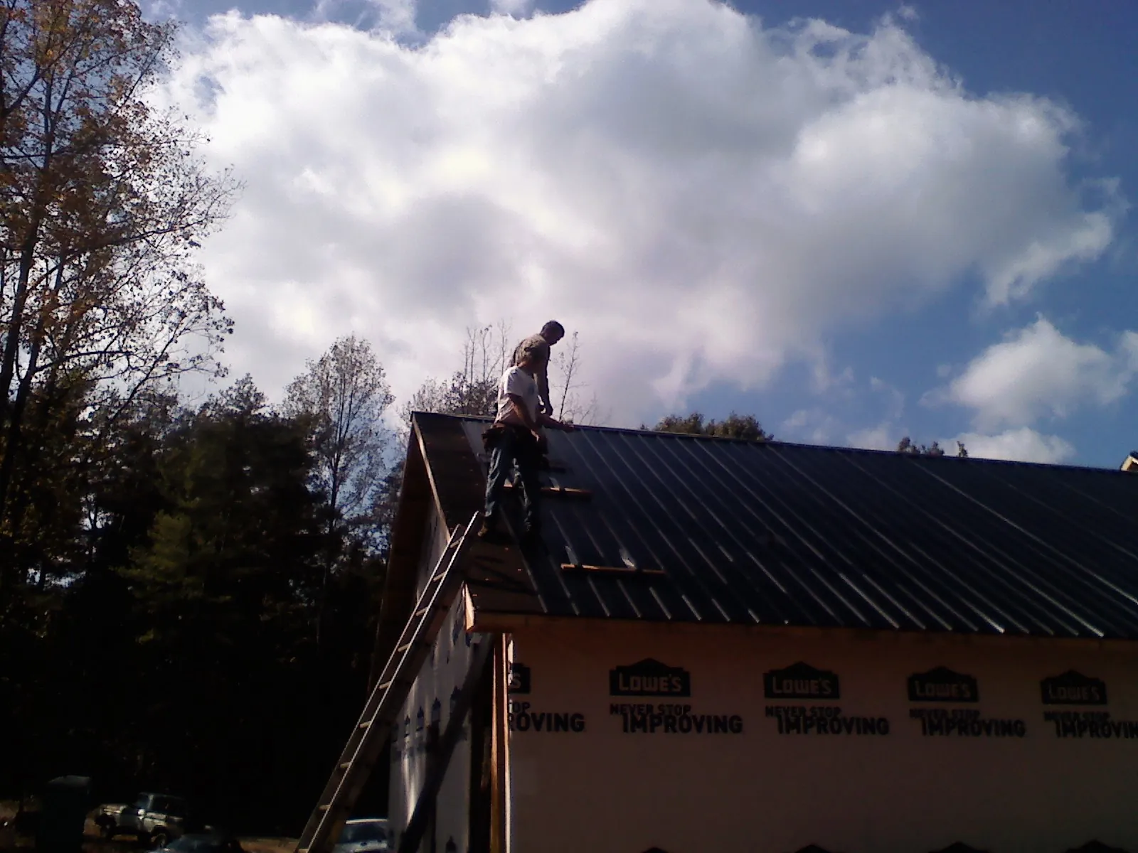 Roofer fastening dark metal panels high against a cloudy sky, from a Roof Inspection job in Maiden