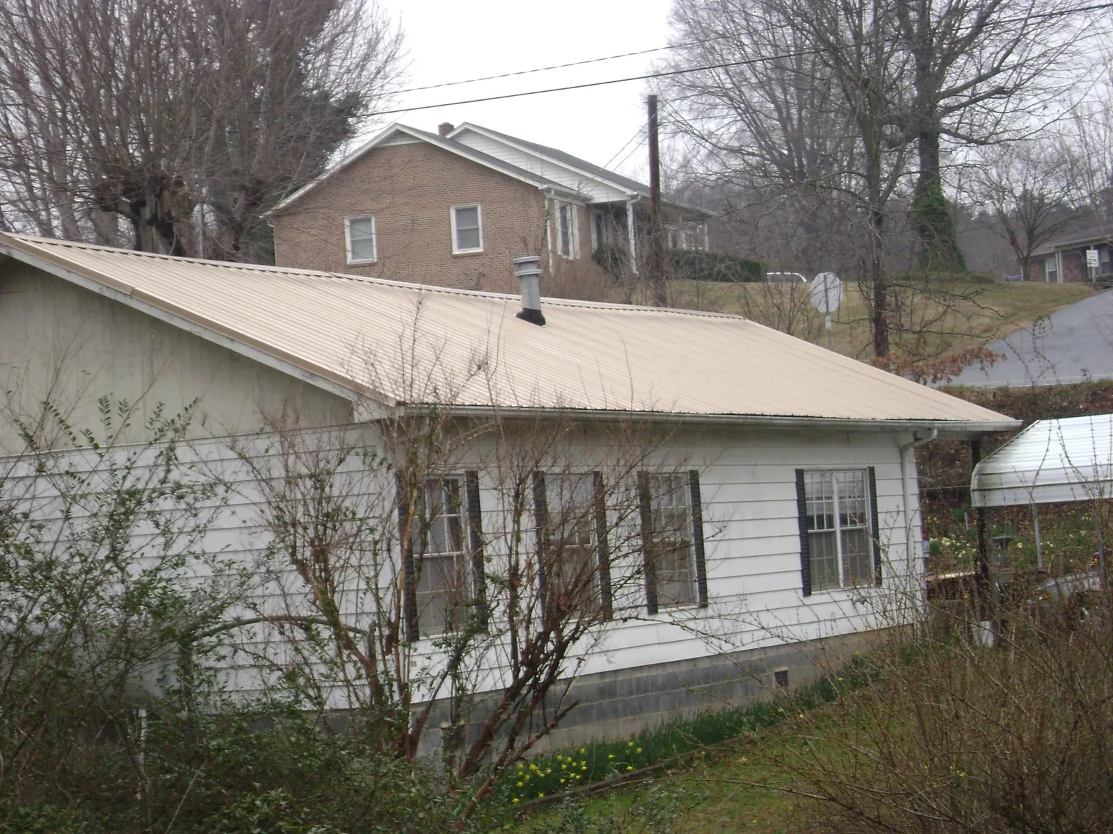 Tan metal roof on a white sided house set into a hillside — Commercial Roofing by Roofing Brothers in Maiden